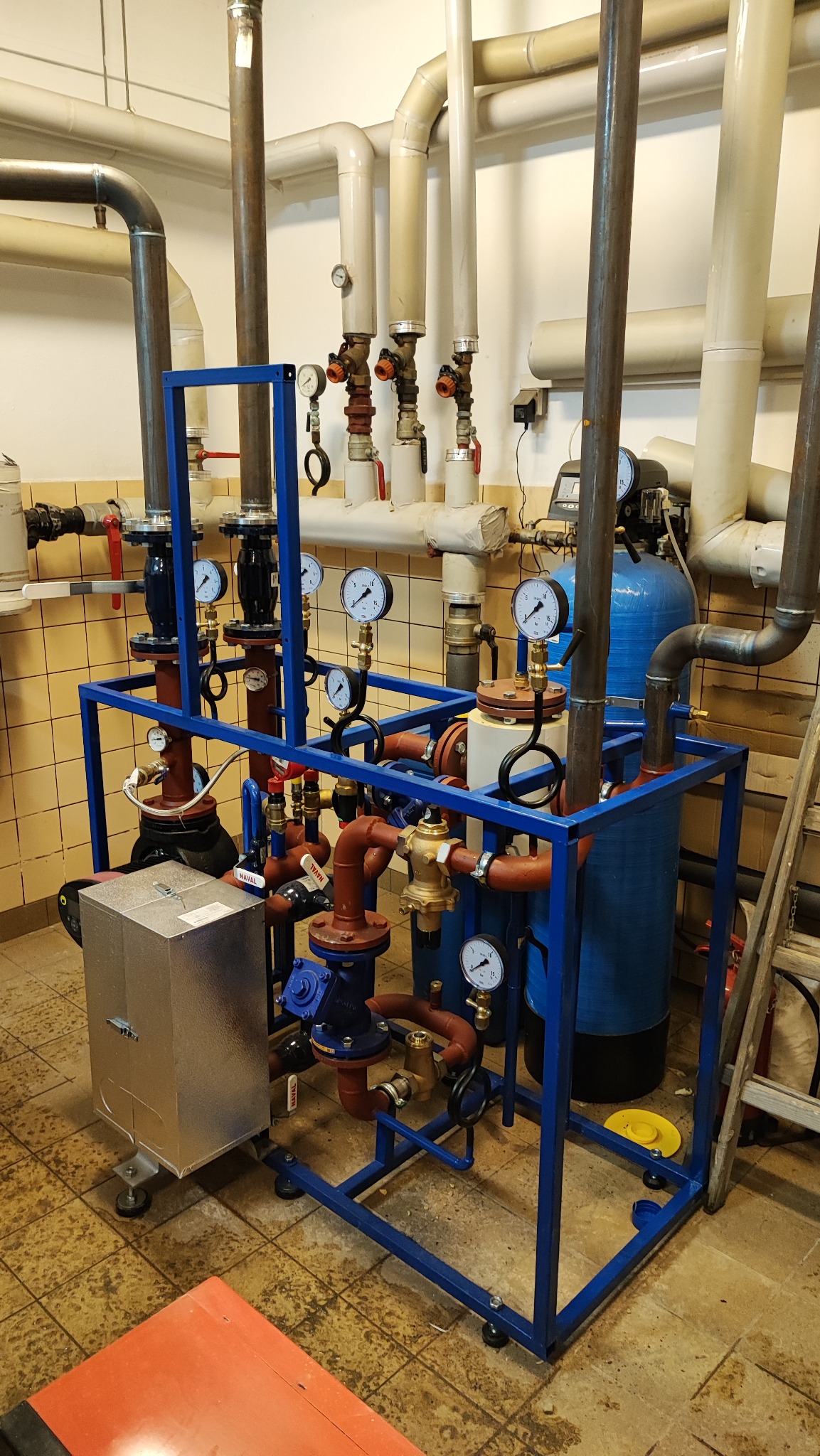 Węzeł cieplny w stalowej ramie z licznymi rurami, zaworami i manometrami, część instalacji grzewczej w kotłowni.