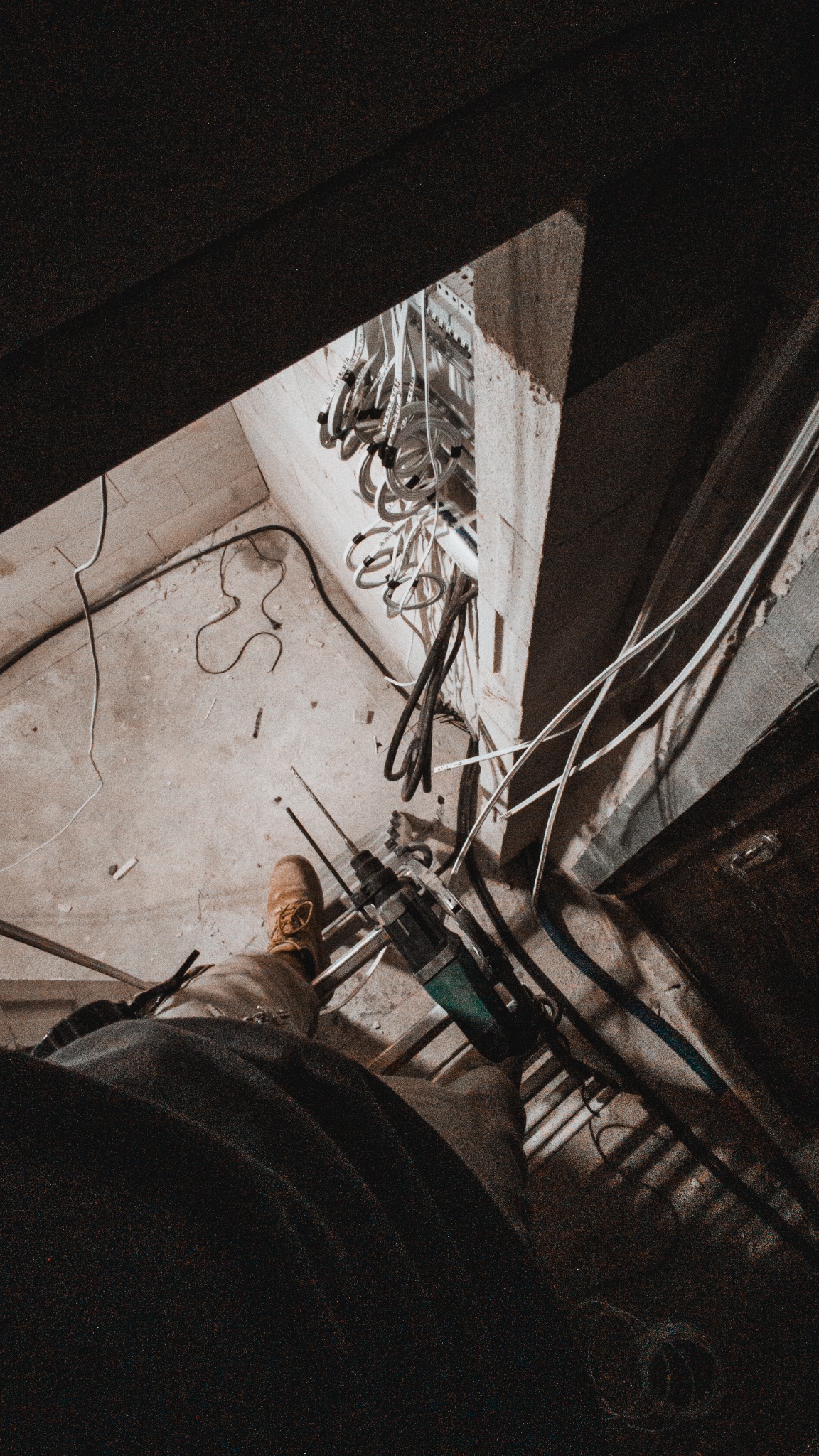 Wnętrze w trakcie prac elektrycznych: widoczne kable, wiertarka udarowa i fragment nogi osoby pracującej. Ujęcie z góry, surowy stan wykończenia.