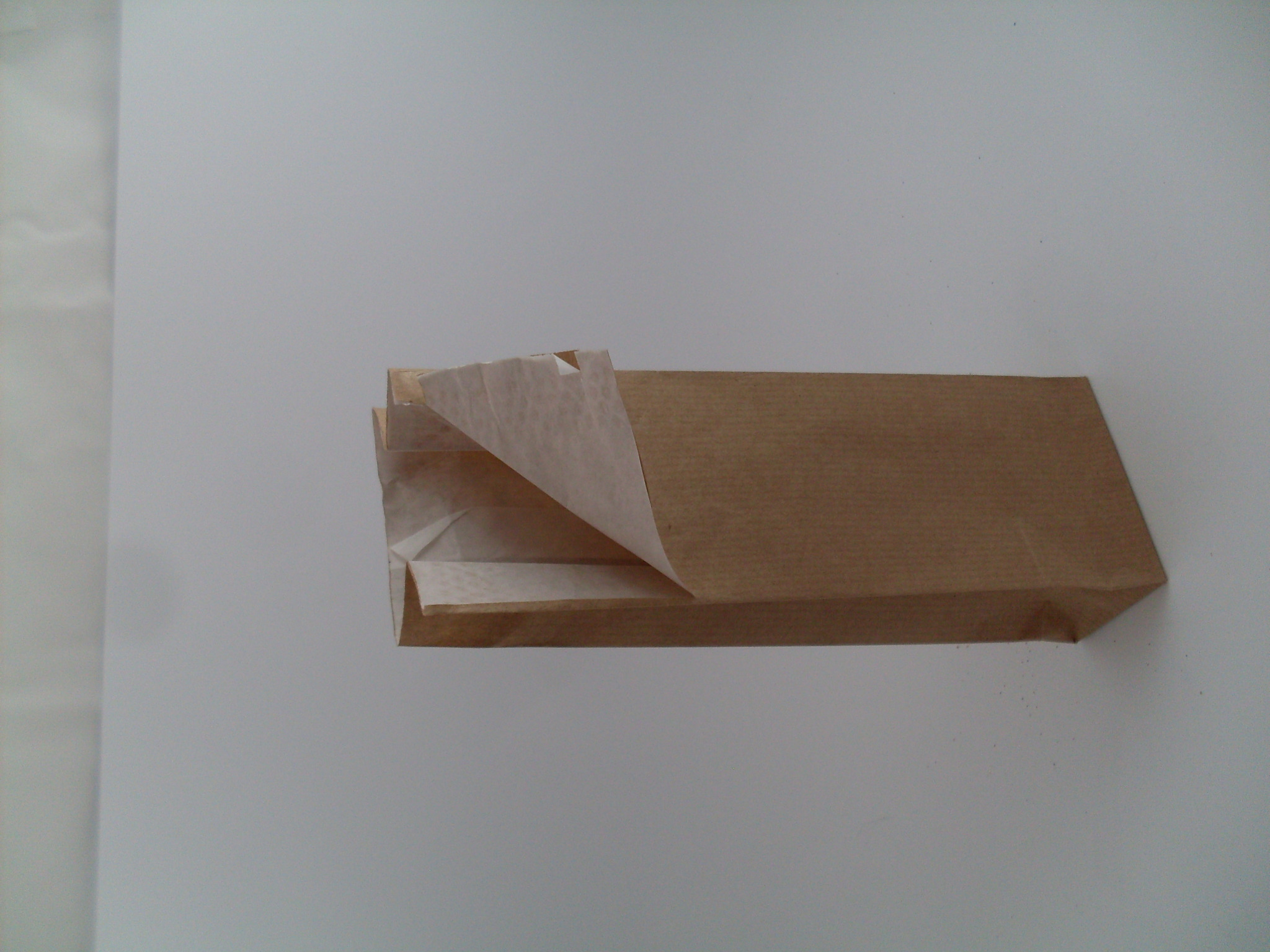 Otwarta papierowa torebka z brązowego papieru kraft, wyłożona białym pergaminem, leżąca na białym tle.