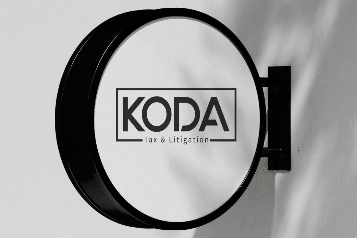 Okrągły szyld z czarną obwódką, zamontowany na ścianie, prezentuje logo 'KODA' w czarnej ramce, z napisem 'Tax & Litigation' poniżej.