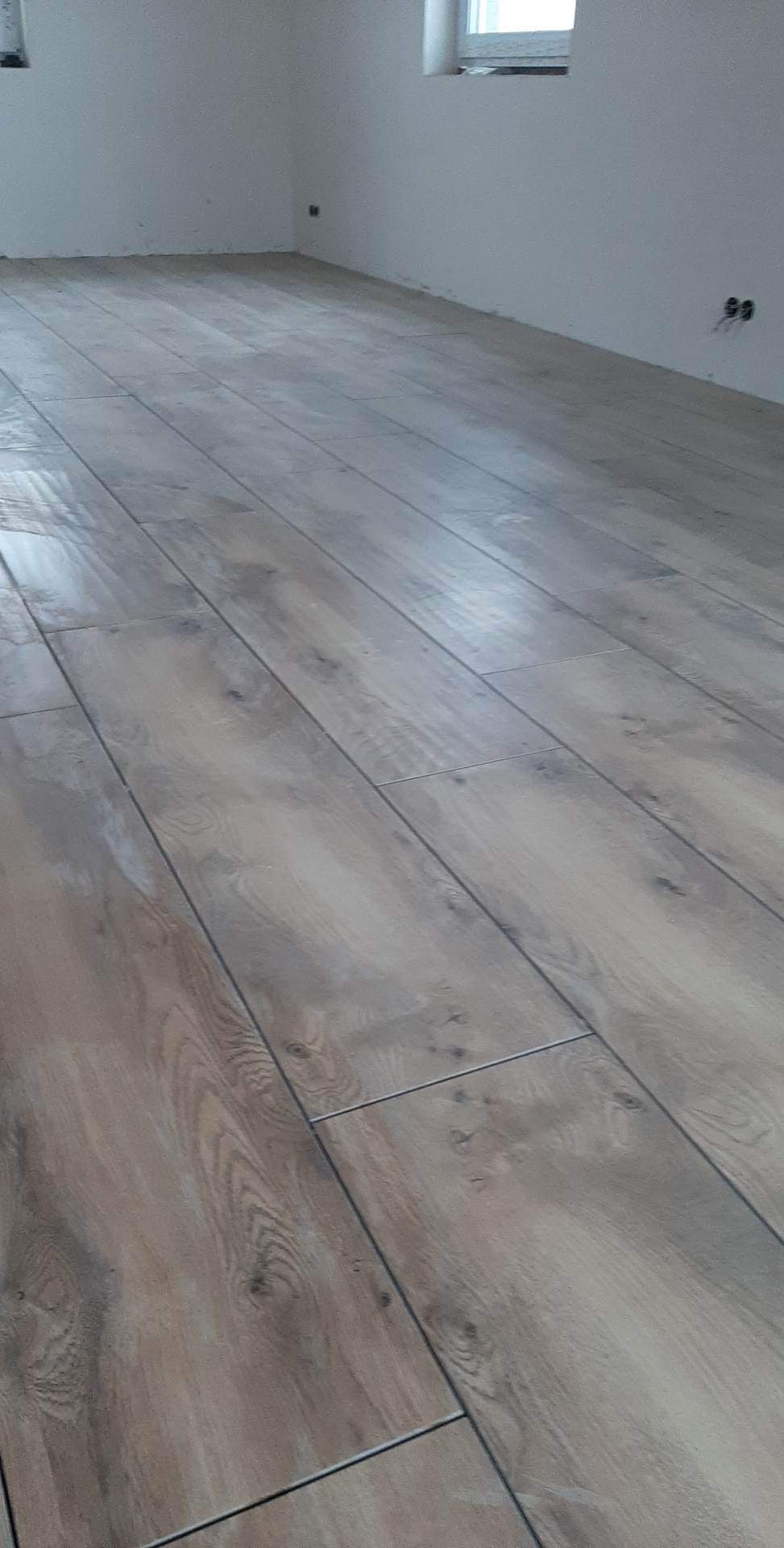 Ułożone panele podłogowe w jasnym odcieniu drewna, widoczne fugi i fragment ściany z gniazdkami elektrycznymi.