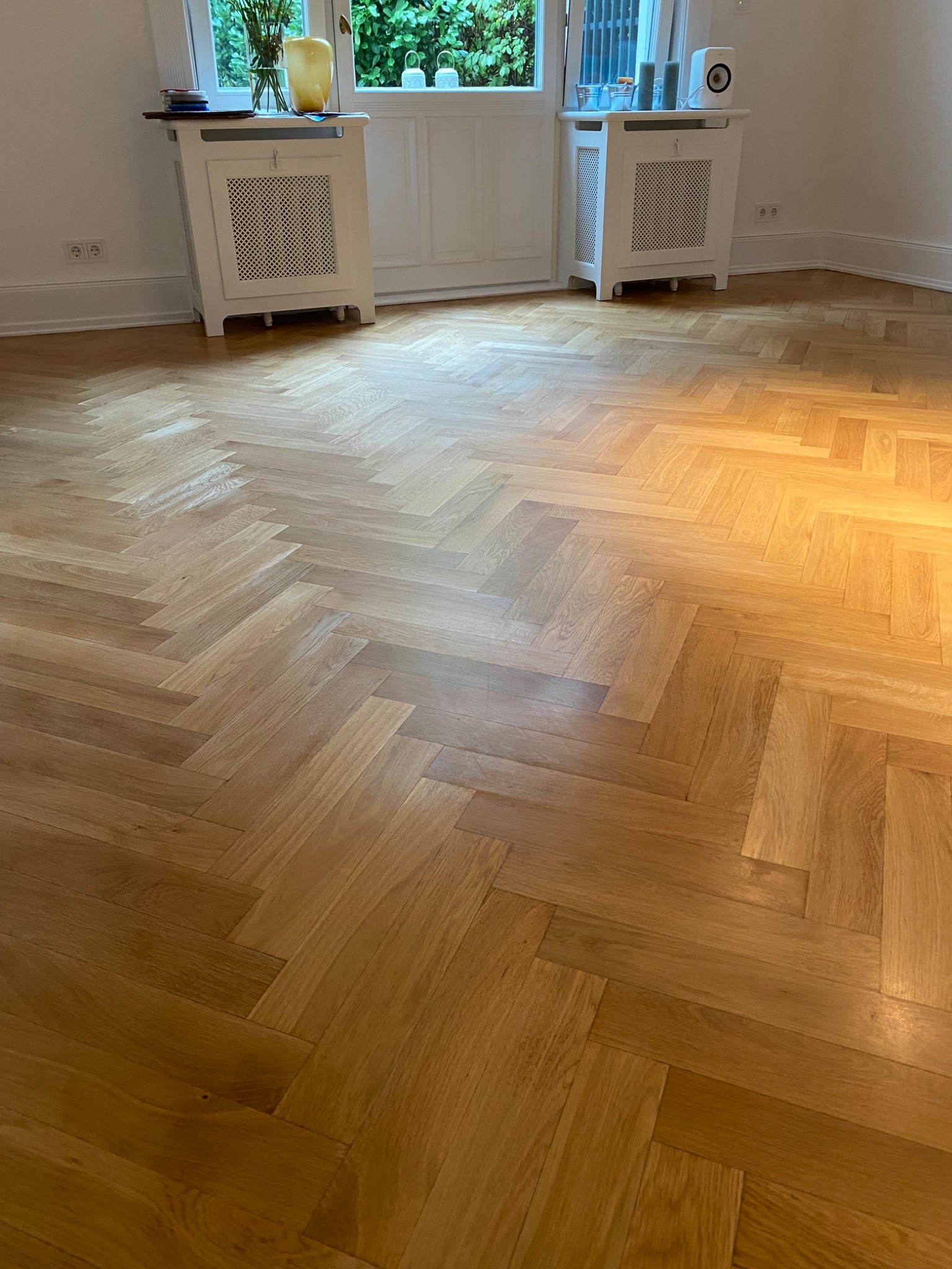 Ułożony parkiet w jodełkę francuską z widocznymi grzejnikami pod oknami.