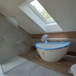 Nowa, owalna wanna zabezpieczona folią i niebieską taśmą malarską w łazience na poddaszu ze skośnym oknem dachowym, obok kabina prysznicowa ze szklaną ścianką.