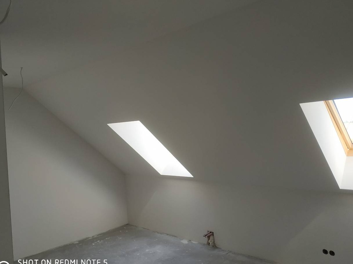 Poddasze po malowaniu na biało z dwoma oknami dachowymi, widoczne ślady po pracach wykończeniowych na podłodze.