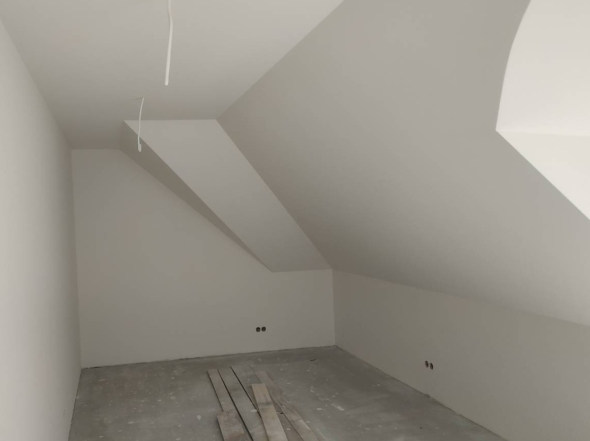 Poddasze po szpachlowaniu i malowaniu na biało, widoczne kable wystające z sufitu i listwy przypodłogowe na podłodze.