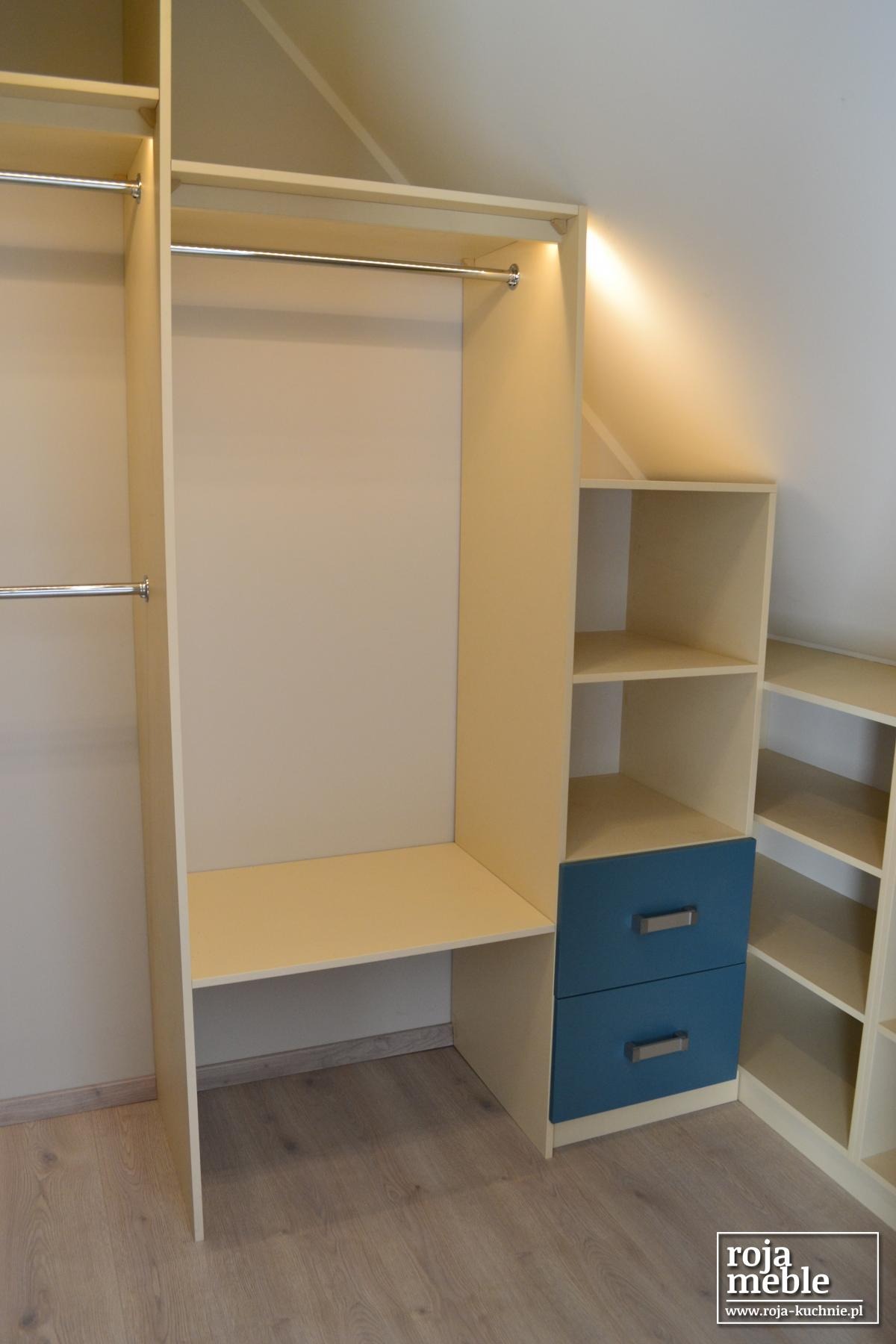 Jasna szafa wnękowa z drążkami i niebieskimi szufladami, dopasowana do skosu dachu, zrealizowana w Starym Polu.