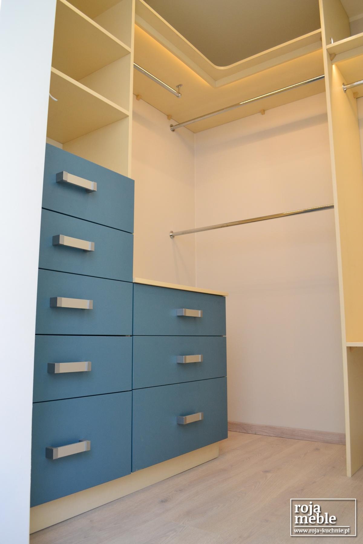 Wnętrze szafy wnękowej z niebieskimi szufladami i oświetleniem LED, widoczne drążki na ubrania i półki.