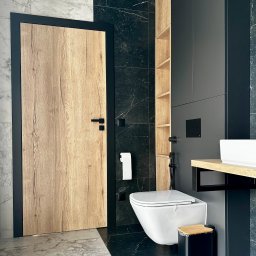 Usługi Stolarskie Ireneusz Kołodziejczyk - Nowoczesna łazienka z drewnianą okleiną drzwi i szafek, czarne płytki marmurowe i biała ceramika sanitarna, minimalistyczny design.