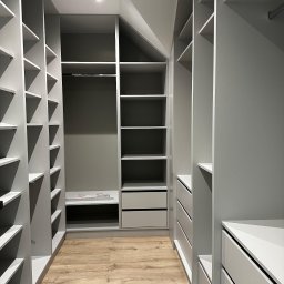 Usługi Stolarskie Ireneusz Kołodziejczyk - Wnętrze garderoby z szarymi szafami wnękowymi z półkami i szufladami, oświetlenie sufitowe, panele podłogowe imitujące drewno.
