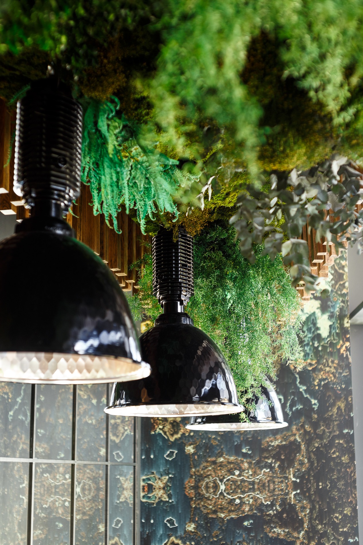 Nowoczesne, czarne lampy wiszące z młotkowaną powierzchnią, zawieszone pod sufitem z elementami roślinnymi, w tle ściana z abstrakcyjnym wzorem.