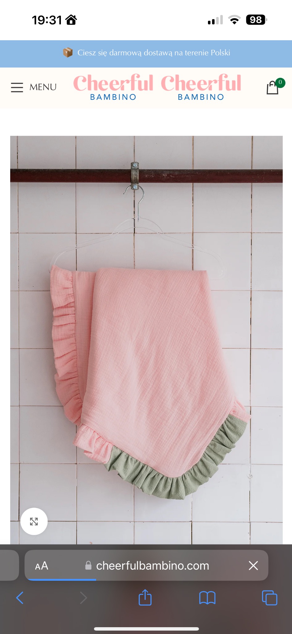 Różowy kocyk dziecięcy z falbanką w kolorze pistacjowym, zawieszony na wieszaku na tle białych płytek.