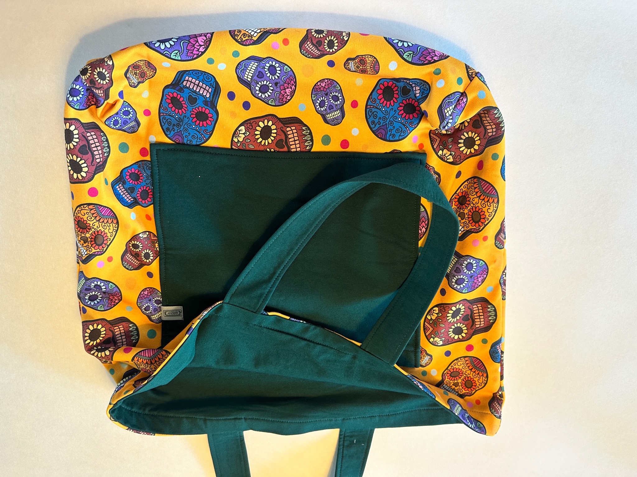 Torba na zakupy z żółtą tkaniną w kolorowe czaszki, z zieloną podszewką i uchwytami, widok z góry.