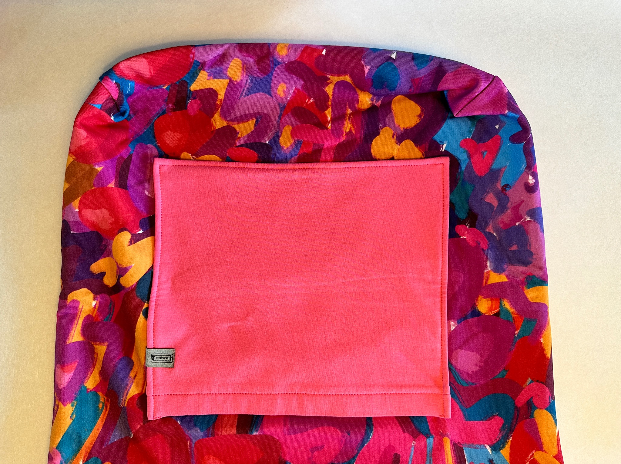 Ukończony pokrowiec z abstrakcyjnym, kolorowym wzorem i różową kieszenią, widoczny z bliska na jasnym tle.