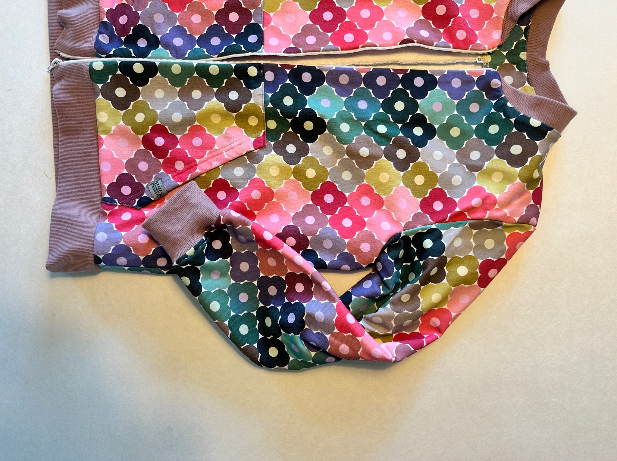 Rozpięta bluza dresowa dziecięca z kolorowym wzorem w kwiaty na jasnym tle, z widocznym zamkiem błyskawicznym i elastycznymi ściągaczami.