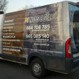 Biały samochód dostawczy z oklejeniem reklamowym firmy Noseda, oferującej transport, wulkanizację i sprzedaż drewna kominkowego, zaparkowany przed salonem sprzedaży.