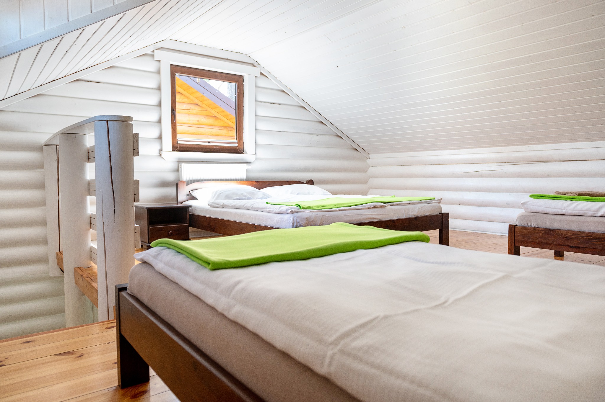 Jasne, drewniane wnętrze pokoju na poddaszu z dwoma łóżkami z zielonymi pledami i spiralnymi schodami.