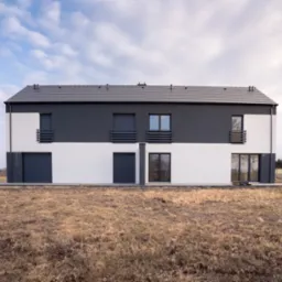 Dwukondygnacyjny dom w nowoczesnym stylu z szarą dachówką, białymi i szarymi ścianami, z dwoma garażami i małymi balkonami, otoczony suchą trawą i błękitnym niebem z chmurami.