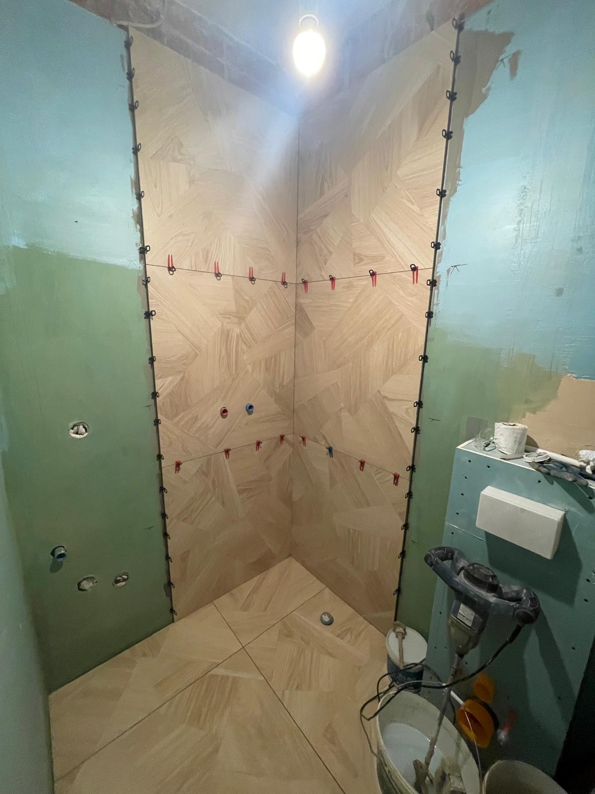 Wnętrze łazienki w trakcie prac wykończeniowych: ułożona podłoga z płytek, ściany przygotowane pod okładzinę, widoczne narzędzia i materiały budowlane.