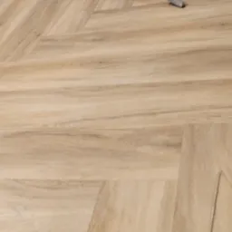 Układanie parkietu w jodełkę, widoczny młotek na świeżo ułożonej podłodze z paneli imitujących drewno.