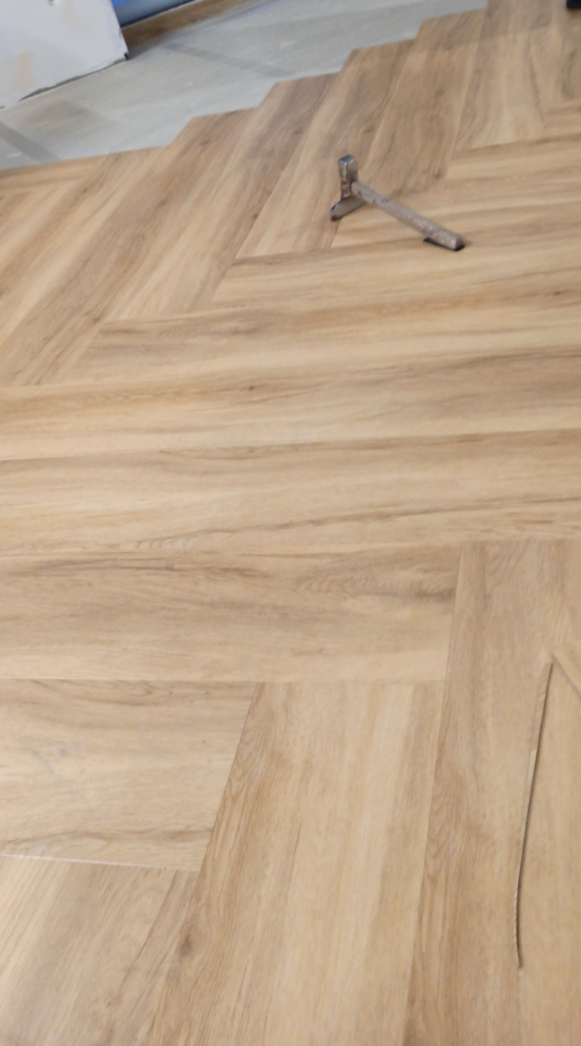 Układanie parkietu w jodełkę, widoczny młotek na świeżo ułożonej podłodze z paneli imitujących drewno.
