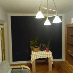 Ściana pomalowana na ciemny granat, z elementami dekoracyjnymi: stolik z serwetą, rośliny w doniczkach i lampa wisząca z trzema kloszami.