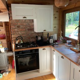 Ganar Robert Śniegóła - Drewniana kuchnia w rustykalnym stylu z białymi szafkami, ceglaną ścianą i piecem na drewno obok piekarnika.