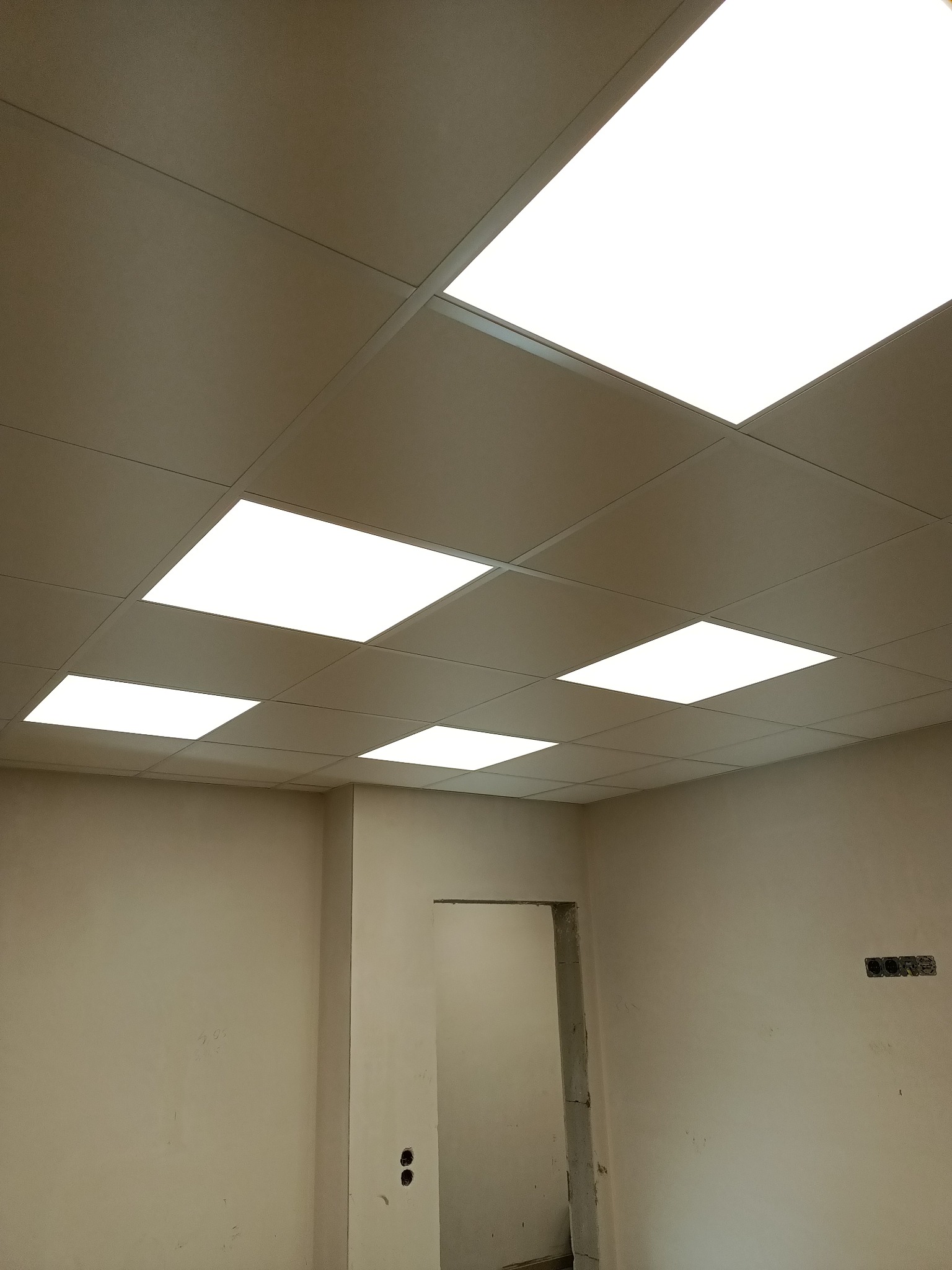 Sufit podwieszany kasetonowy z wbudowanym oświetleniem LED w jasnym biurze przed malowaniem ścian, widoczne puszki elektryczne.