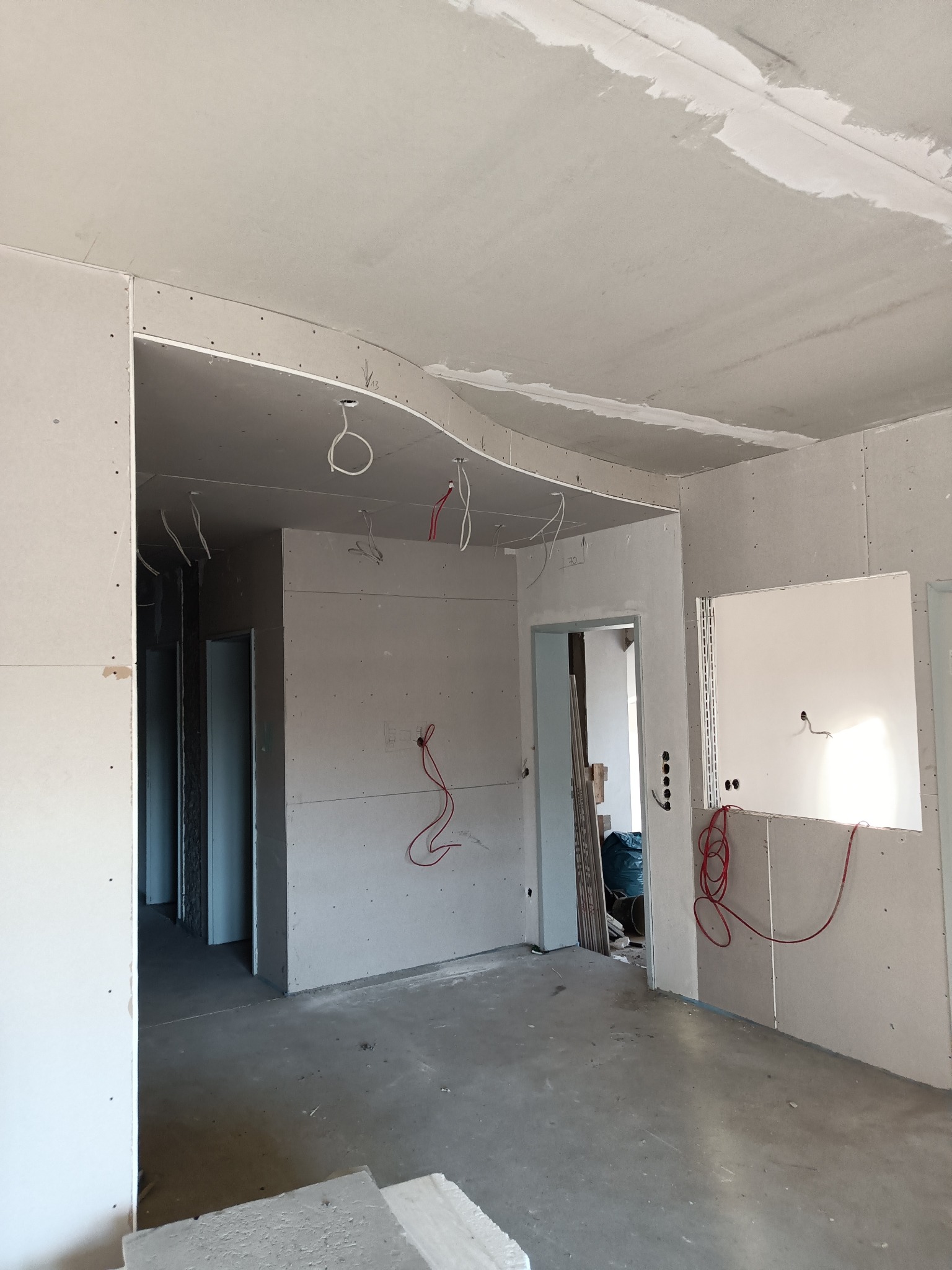 Wnętrze w trakcie montażu płyt kartonowo-gipsowych na ścianach i suficie, widoczne przewody elektryczne, surowy beton na podłodze i częściowo wykończony sufit z widocznymi łączeniami płyt.
