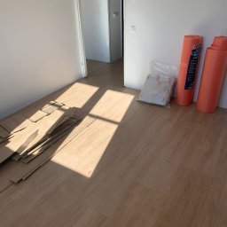 BAHMAL SP. Z.O.O - Układanie paneli podłogowych w jasnym pomieszczeniu, widoczne rozłożone panele, podkład w rolkach oraz wpadające promienie słoneczne.