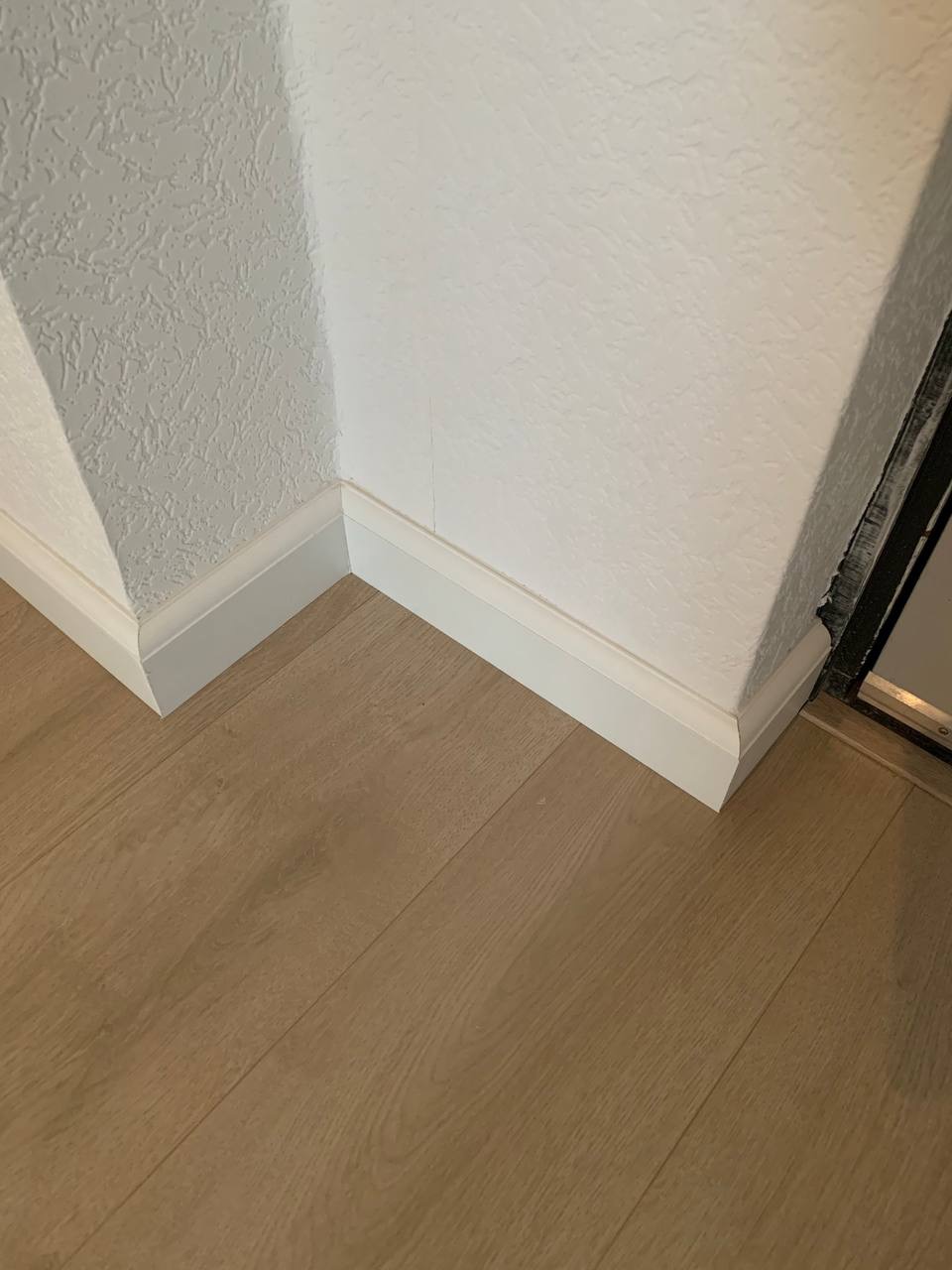 Połączenie ściany z fakturą i podłogi z paneli, wykończone białą listwą przypodłogową w narożniku pomieszczenia.