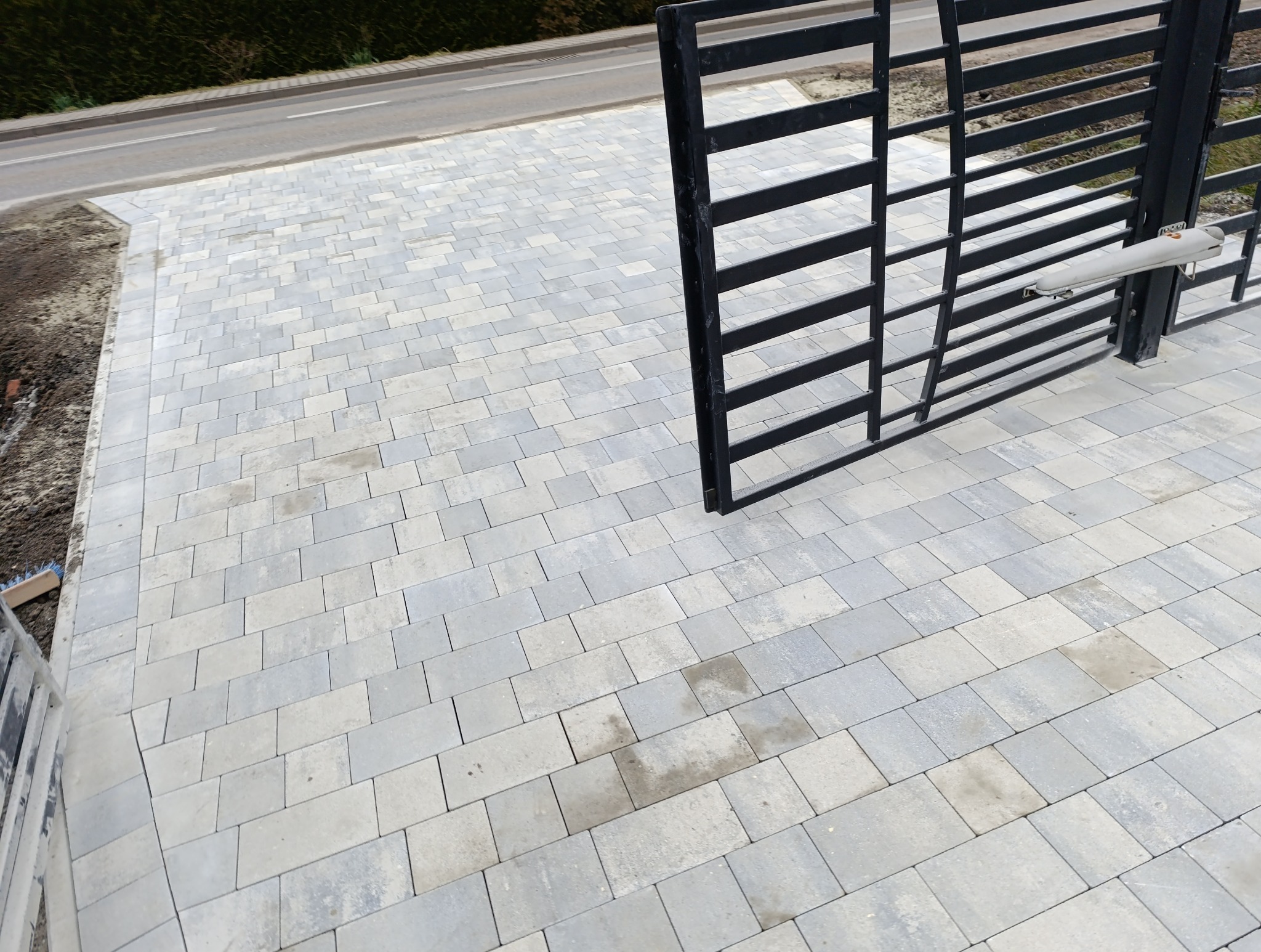 Świeżo ułożona, szara kostka brukowa na podjeździe z automatyczną bramą wjazdową, widok z góry.