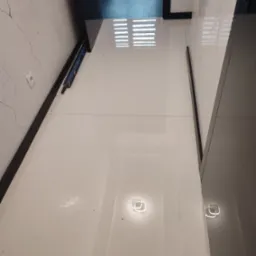 Błyszczące, białe płytki podłogowe po remoncie we Wrocławiu, z widocznym poziomowaniem i fragmentem dekoracyjnej ściany z efektem spękań.