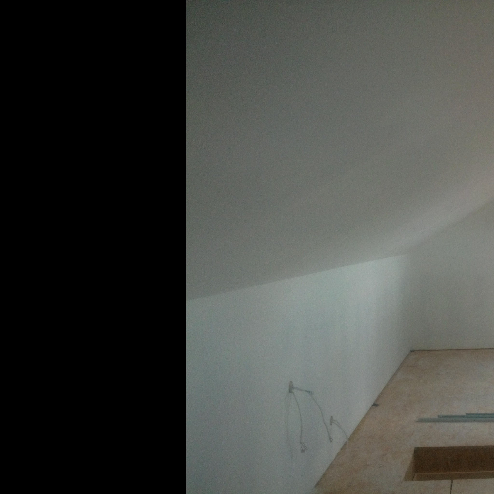 Poddasze w trakcie prac wykończeniowych: surowe ściany, wystające kable elektryczne i fragment widocznej podłogi z elementami konstrukcyjnymi.