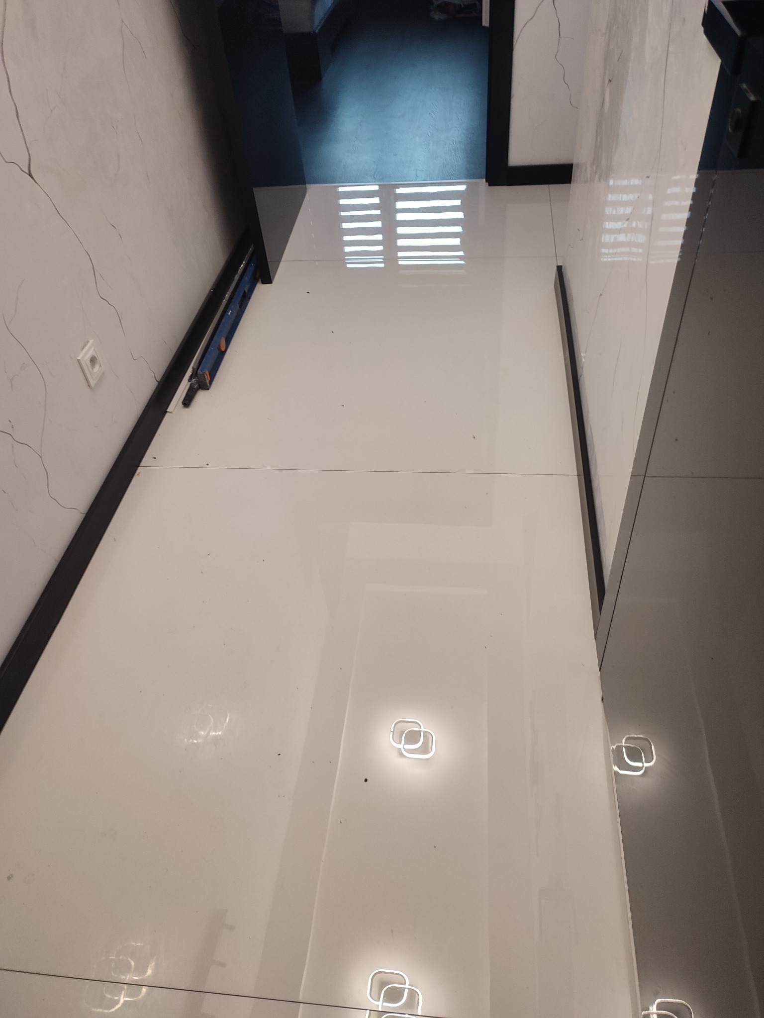 Błyszczące, białe płytki podłogowe po remoncie we Wrocławiu, z widocznym poziomowaniem i fragmentem dekoracyjnej ściany z efektem spękań.