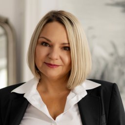 BLACKROOK INVEST SPÓŁKA Z OGRANICZONĄ ODPOWIEDZIALNOŚCIĄ - Portret kobiety w czarnej marynarce i białej koszuli, z blond włosami do ramion, patrzącej w obiektyw. W tle widoczne lustro i abstrakcyjny obraz.