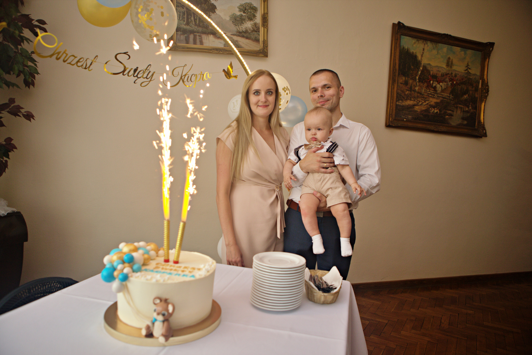 Rodzina pozuje do zdjęcia podczas uroczystości, w tle dekoracje, tort z fontannami iskier