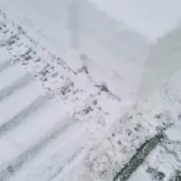 Krawędź odśnieżonej powierzchni z wyraźnymi śladami opon na śniegu, obok wysoki pryzmat śniegu.