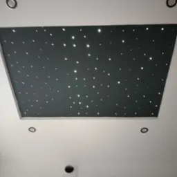 Czarny sufit podwieszany z efektem gwieździstego nieba, otoczony białym sufitem z widocznymi punktami oświetleniowymi.