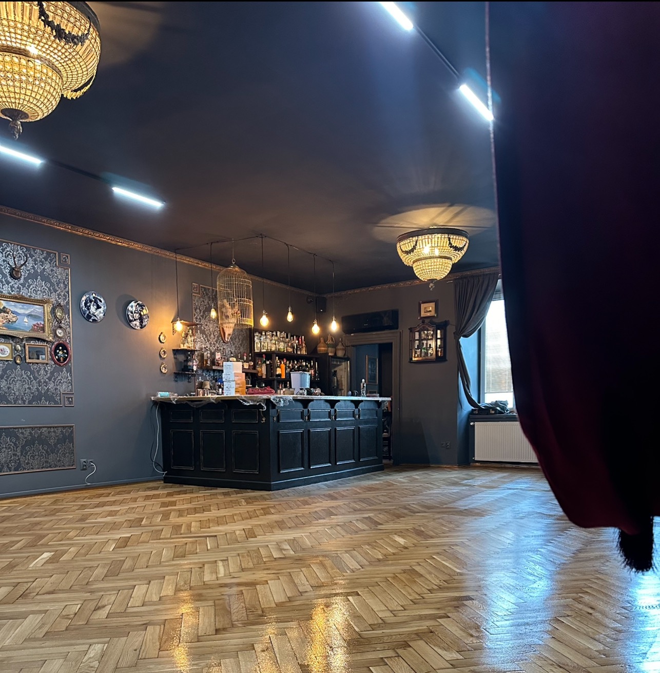 Parkiet ułożony w jodełkę francuską w eleganckim wnętrzu baru z ciemnymi ścianami, ozdobnymi elementami i stylowym oświetleniem.