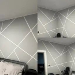 Ściana w pokoju w Jaworze pomalowana na szaro z białymi, geometrycznymi wzorami, widoczne ł&oacute;żko i krzesło.