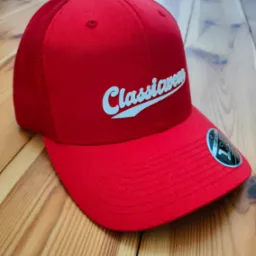 Czerwona czapka typu trucker z białym napisem 'Classicwear' leżąca na drewnianej podłodze.