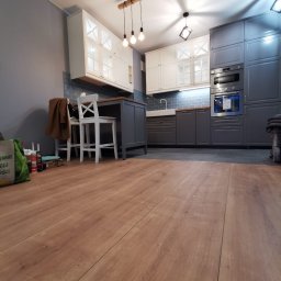 Smart Interiors - Nowoczesna kuchnia w odcieniach szarości i bieli z drewnianym blatem, widok z poziomu podłogi na panele, oświetlenie punktowe i wiszące żarówki.