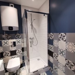 Smart Interiors - Nowoczesna łazienka z kabiną prysznicową, wiszącą toaletą i wzorzystymi płytkami w odcieniach szarości i błękitu, z widocznym bojlerem elektrycznym na ścianie.