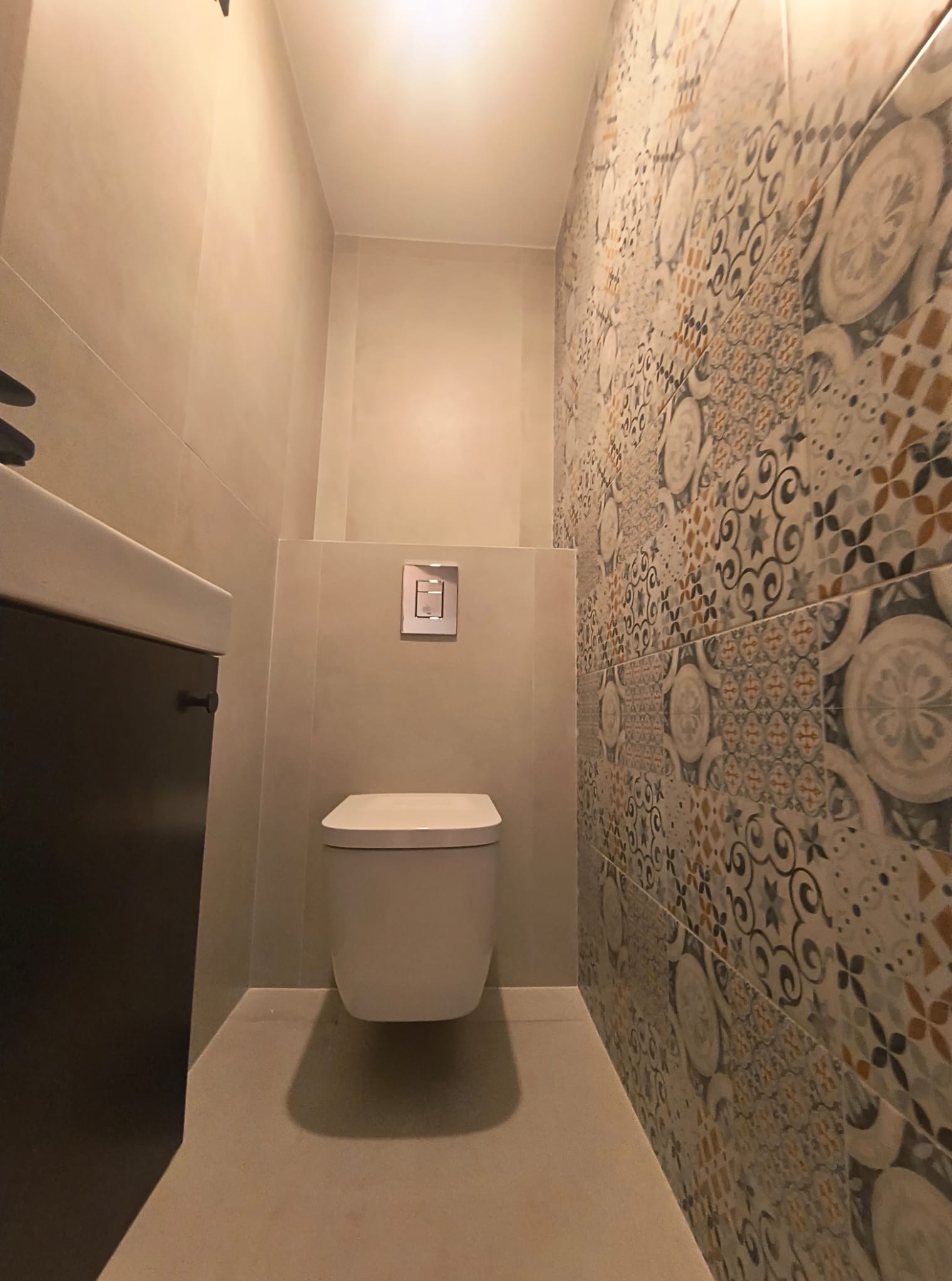 Nowoczesna łazienka z podwieszaną toaletą, beżowymi ścianami i dekoracyjnymi płytkami na jednej ścianie, widok z dołu podkreśla minimalizm wnętrza.