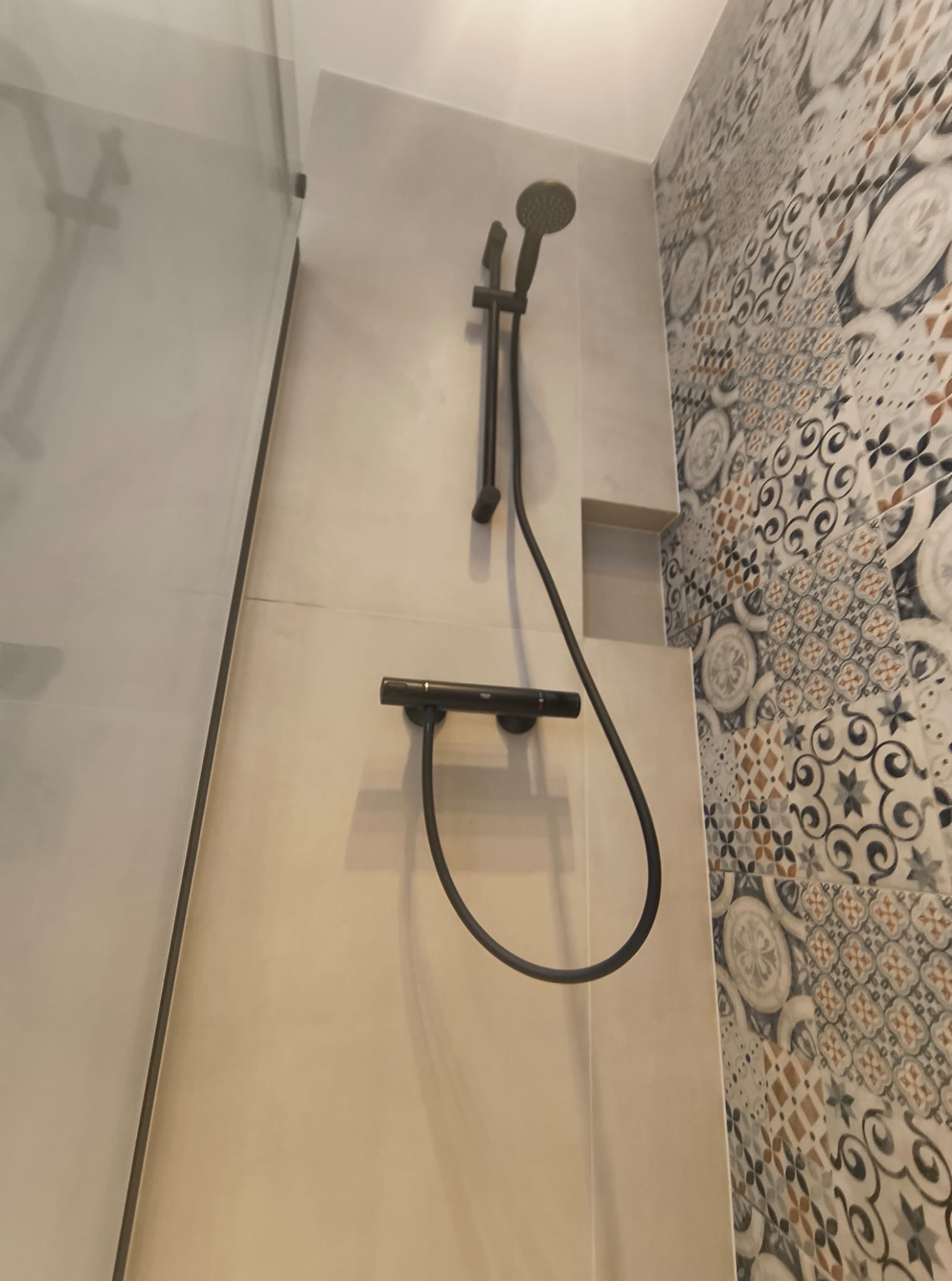 Nowoczesna kabina prysznicowa z czarną armaturą i dekoracyjnymi płytkami ceramicznymi na ścianie, widok z dołu.