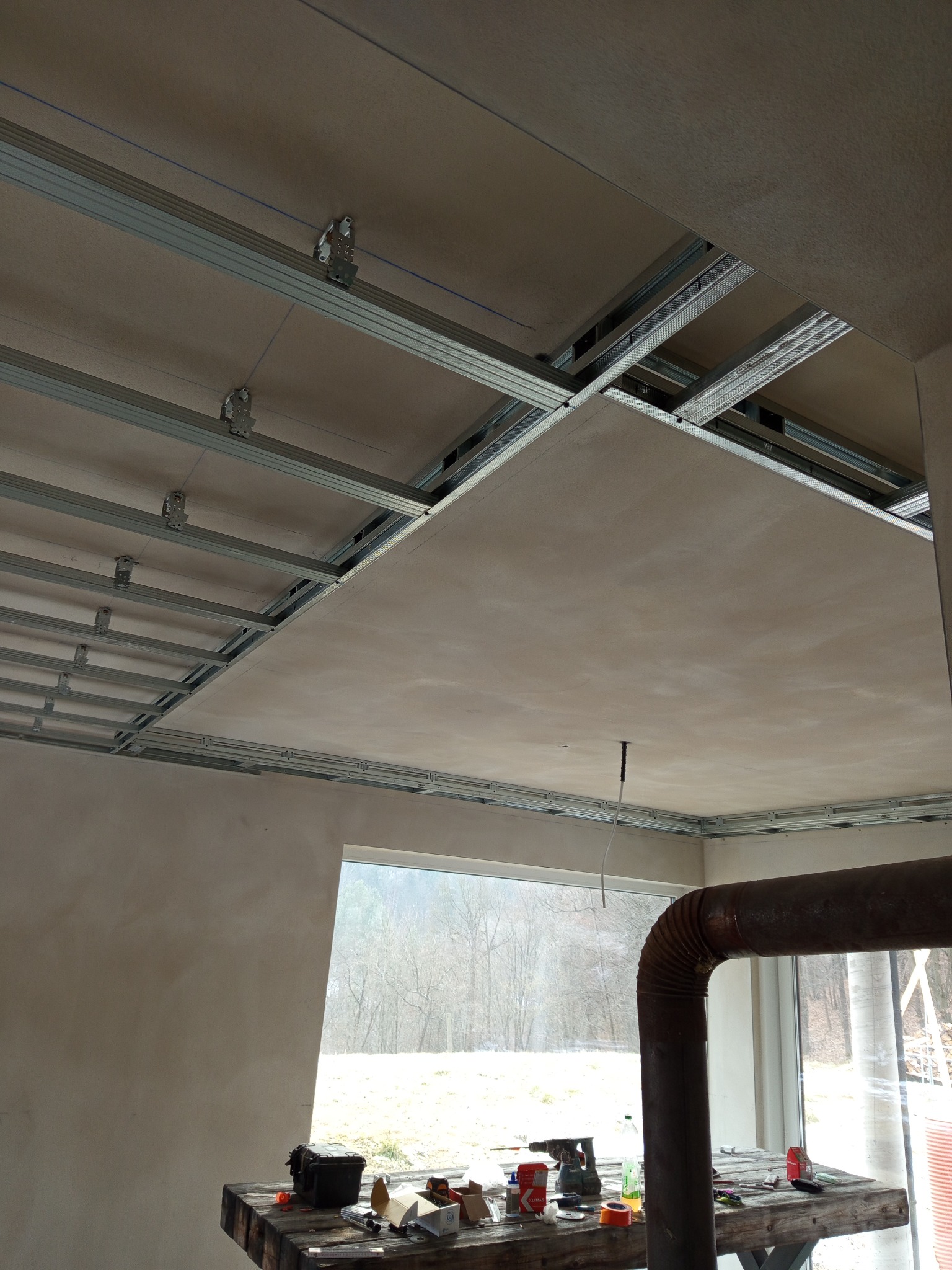 Montaż płyty karton gips na metalowym stelażu sufitu w Rudniku, widoczne narzędzia i materiały na stole roboczym.