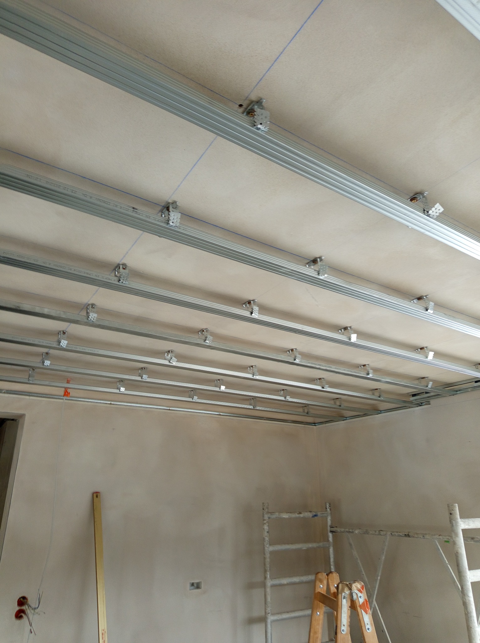 Metalowy stelaż pod konstrukcję sufitu, przymocowany do istniejącego sufitu, widoczne przewody elektryczne, drabiny malarskie
