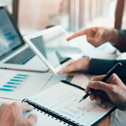 CENTRUM KSIĘGOWO-EKONOMICZNE LUB Sp. z o.o. - Dwie osoby analizują dane finansowe na laptopie i tablecie, notując w notesie, widoczne wykresy i liczby.