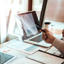 CENTRUM KSIĘGOWO-EKONOMICZNE LUB Sp. z o.o. - Analiza raportu na laptopie z wykresem słupkowym, dokumenty, notatnik i kawa na biurku w jasnym biurze.