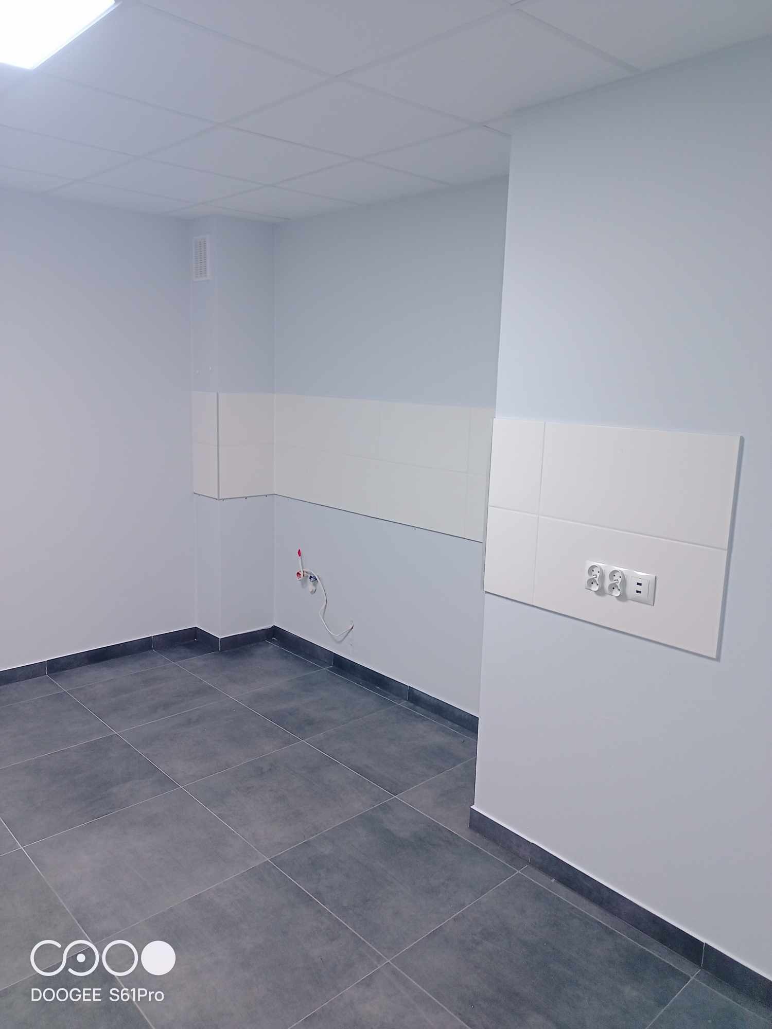 Wykończone wnętrze biura z szarą podłogą z płytek, białymi panelami ściennymi z gniazdkami elektrycznymi oraz białym sufitem podwieszanym.